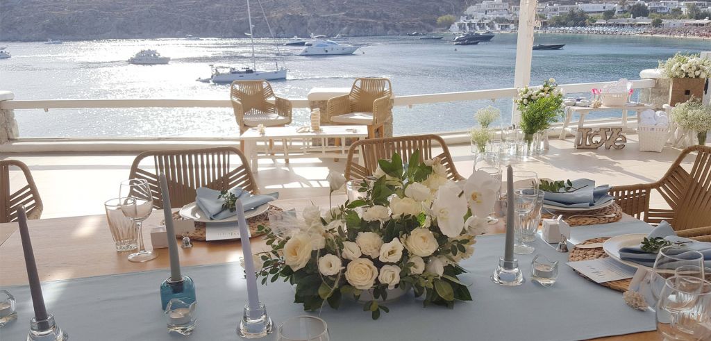 A large wedding table adorned with a baby blue runner and a composition of white roses at Phos Restaurant