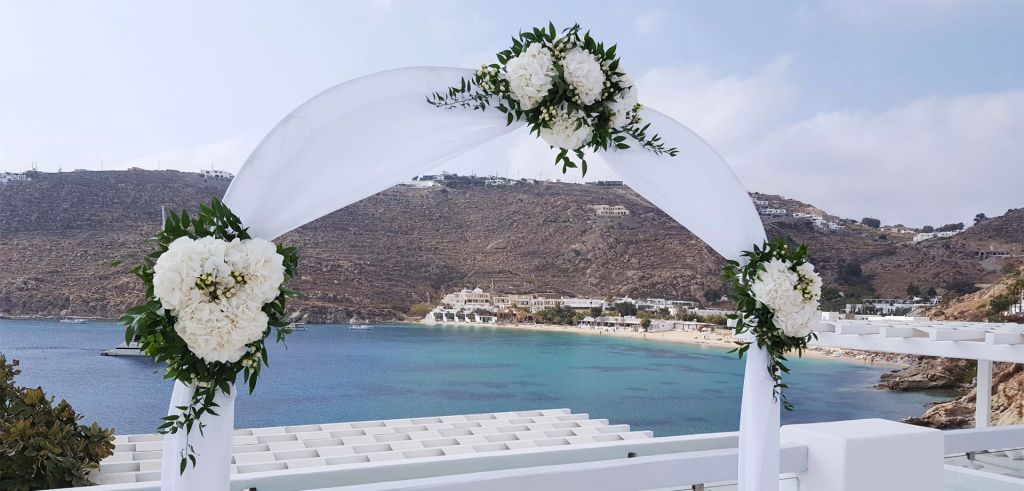 A wedding arch made of white fabrics and adorned with white flowers.