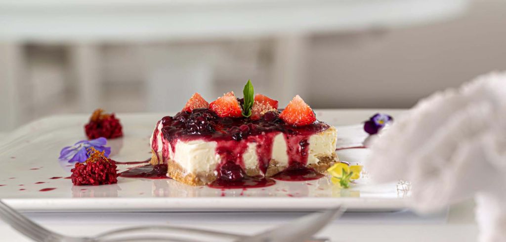 A gastronomic dish featuring cheesecake adorned with raspberries and strawberries, served at Phos Restaurant