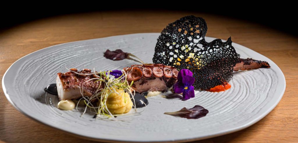 A delectable gourmet dish highlighting octopus and adorned with edible flowers, served at Phos Restaurant.